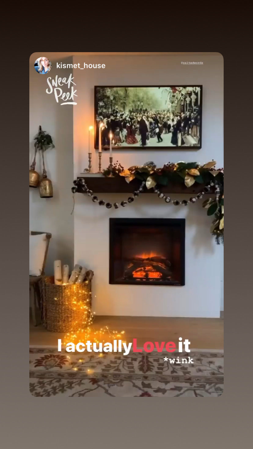 Framed wall art above fireplace with floral garland and string lights