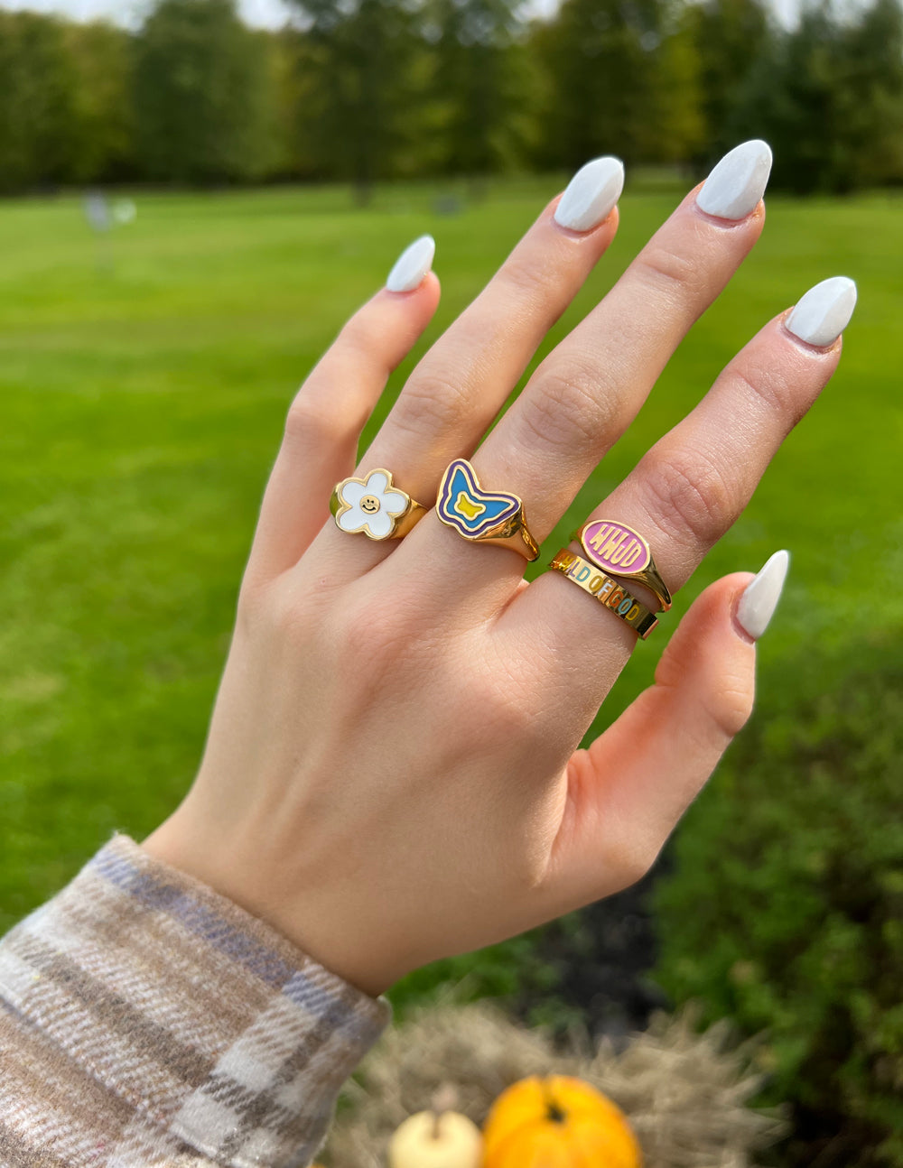 Smiley flower ring with white enamel petals on a gold band, on finger