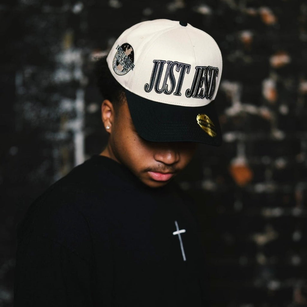 Cream and black snapback cap with embroidered "JUST JESUS" logo on front.