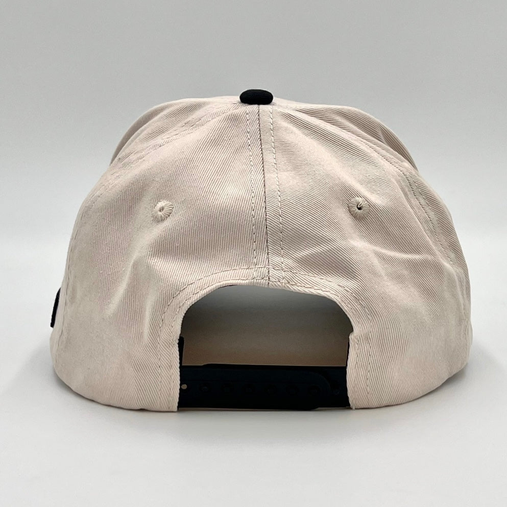Cream snapback cap back view with adjustable strap; black underbrim.
