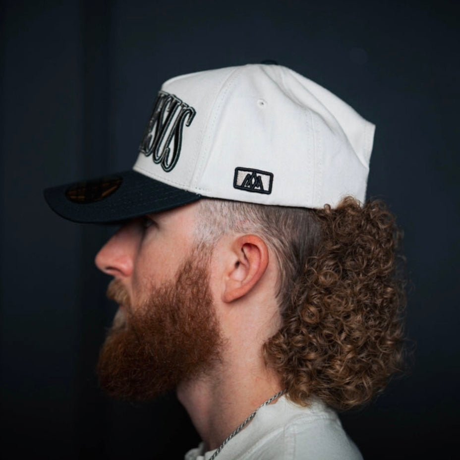 Cream snapback cap side/back view with black embroidered logo and patch.