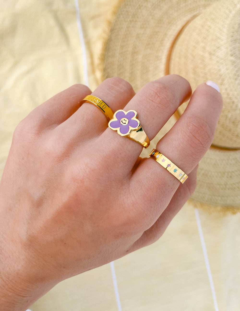 Gold-tone ring with small lavender smiley flower face on a hand