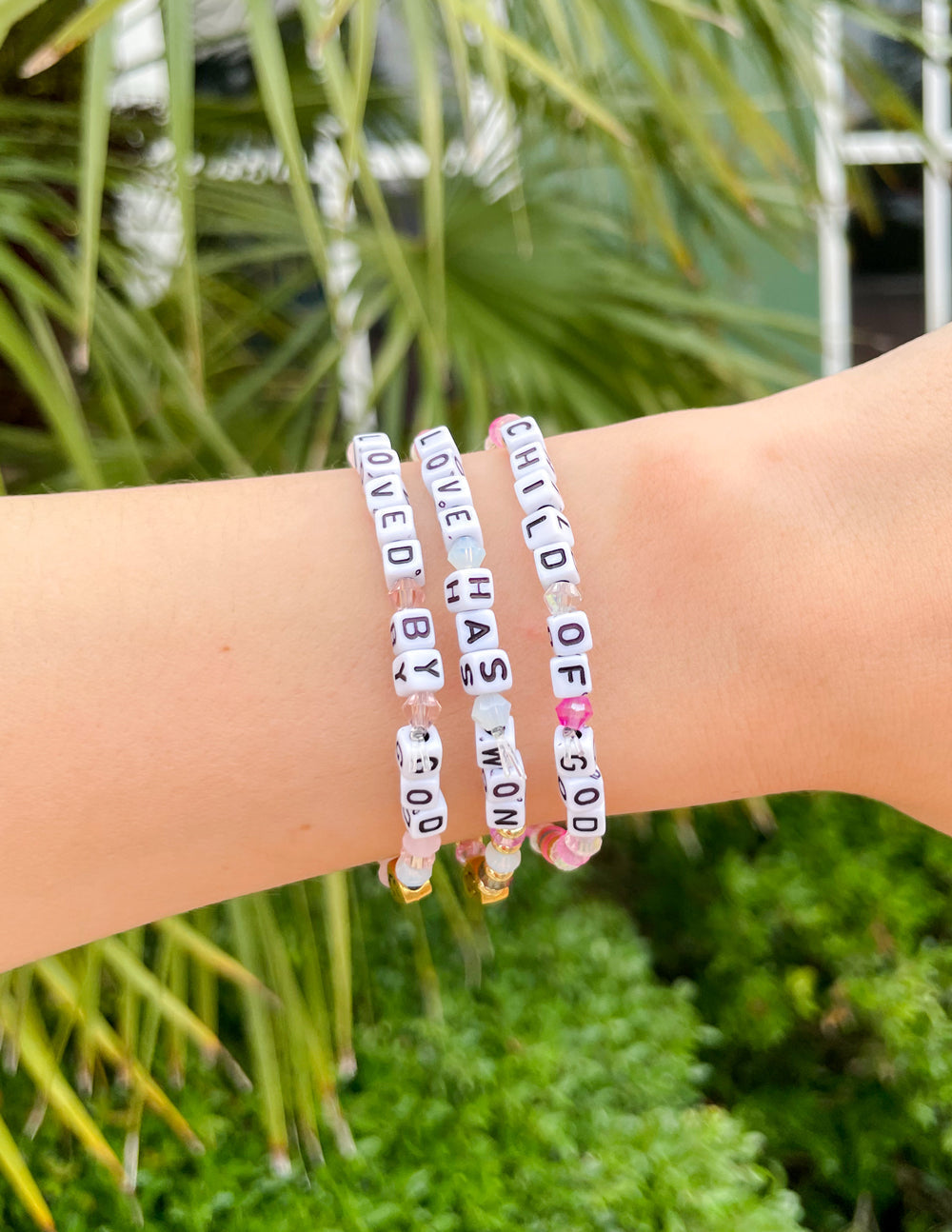 Stack of letter bracelets on wrist with white beads and colorful letter tiles