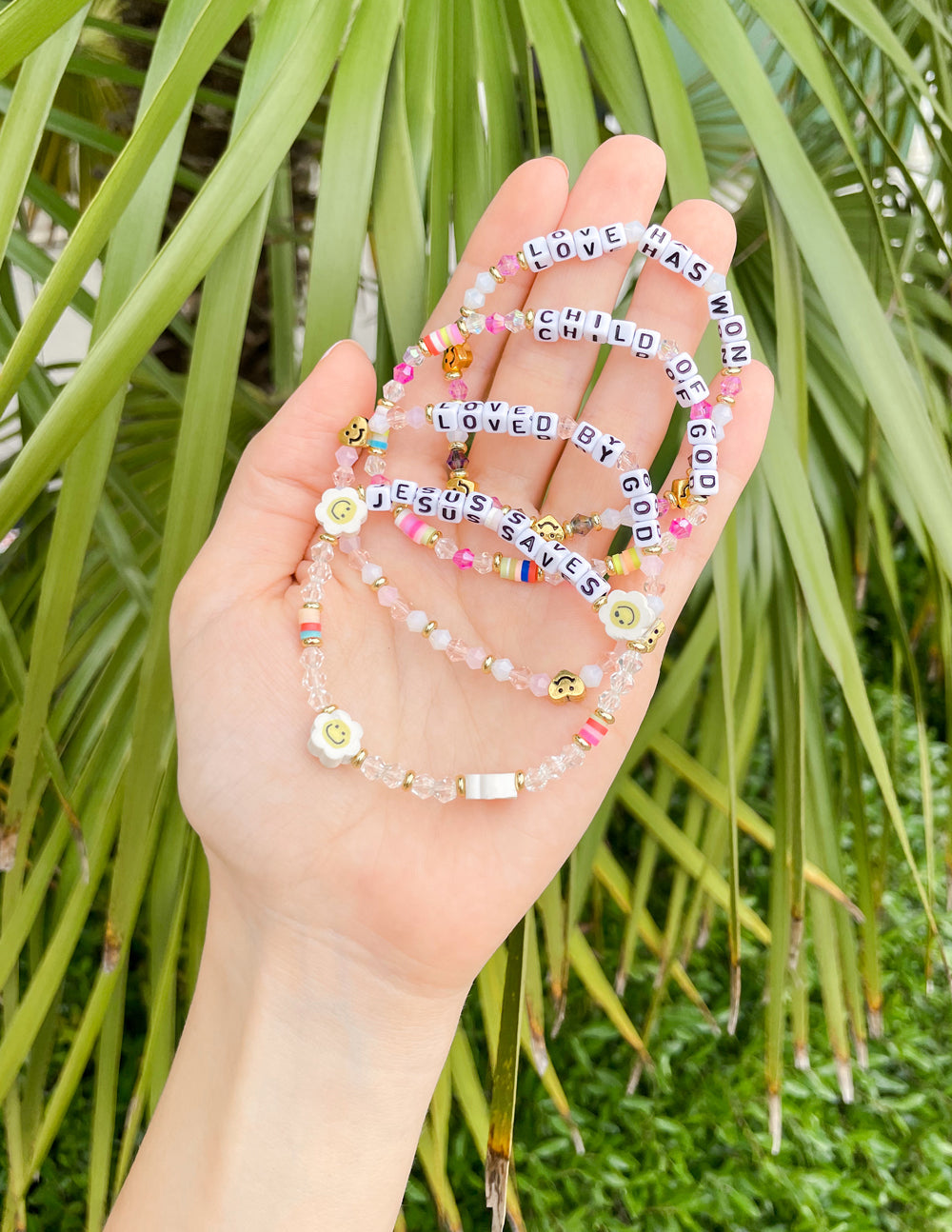 Set of beaded letter bracelets held in hand with pink and gold beads showing love text.