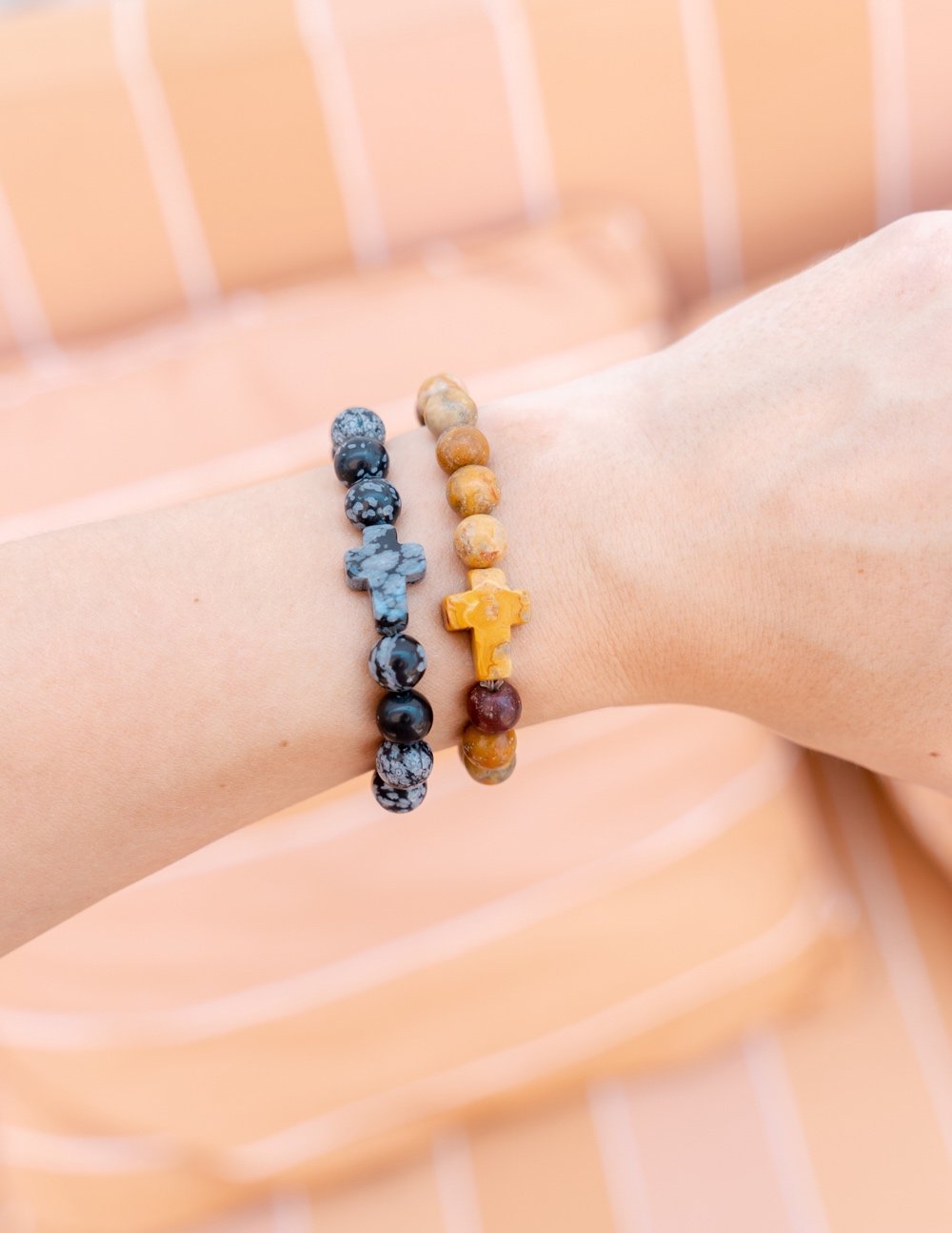 Stone bead bracelet with dark beads and yellow cross charm, worn on wrist