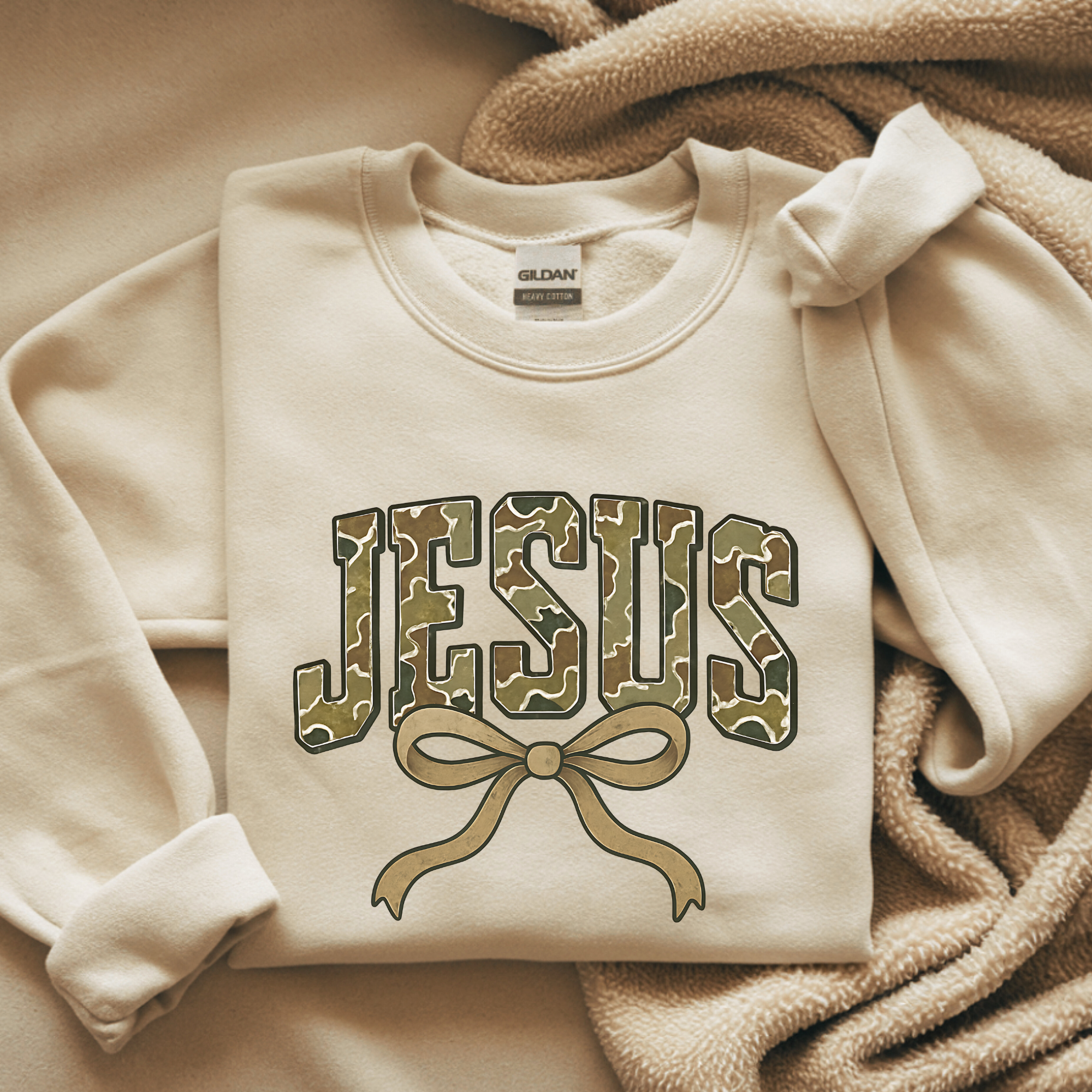 Cream crewneck sweatshirt with camouflage-style 'Jesus' graphic and bow