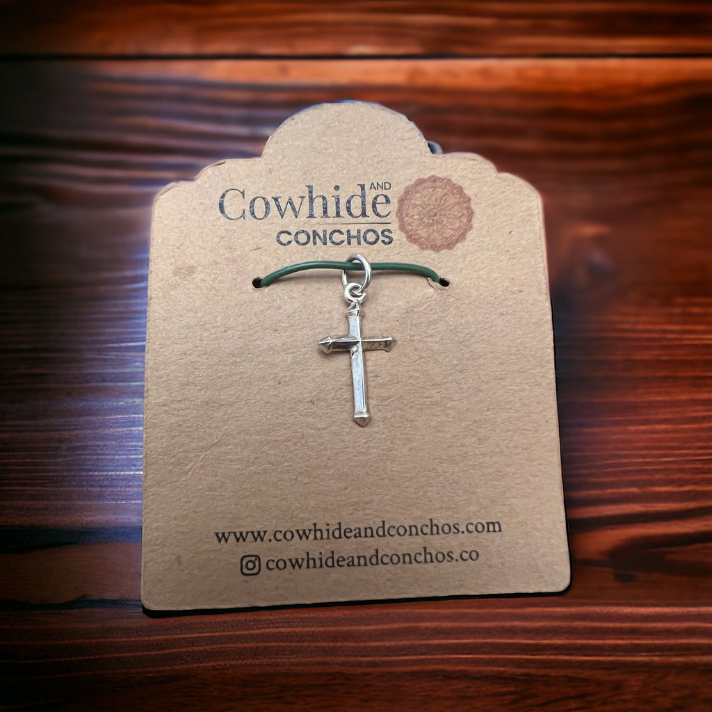 Sterling silver cross charm on green cord, displayed on a card