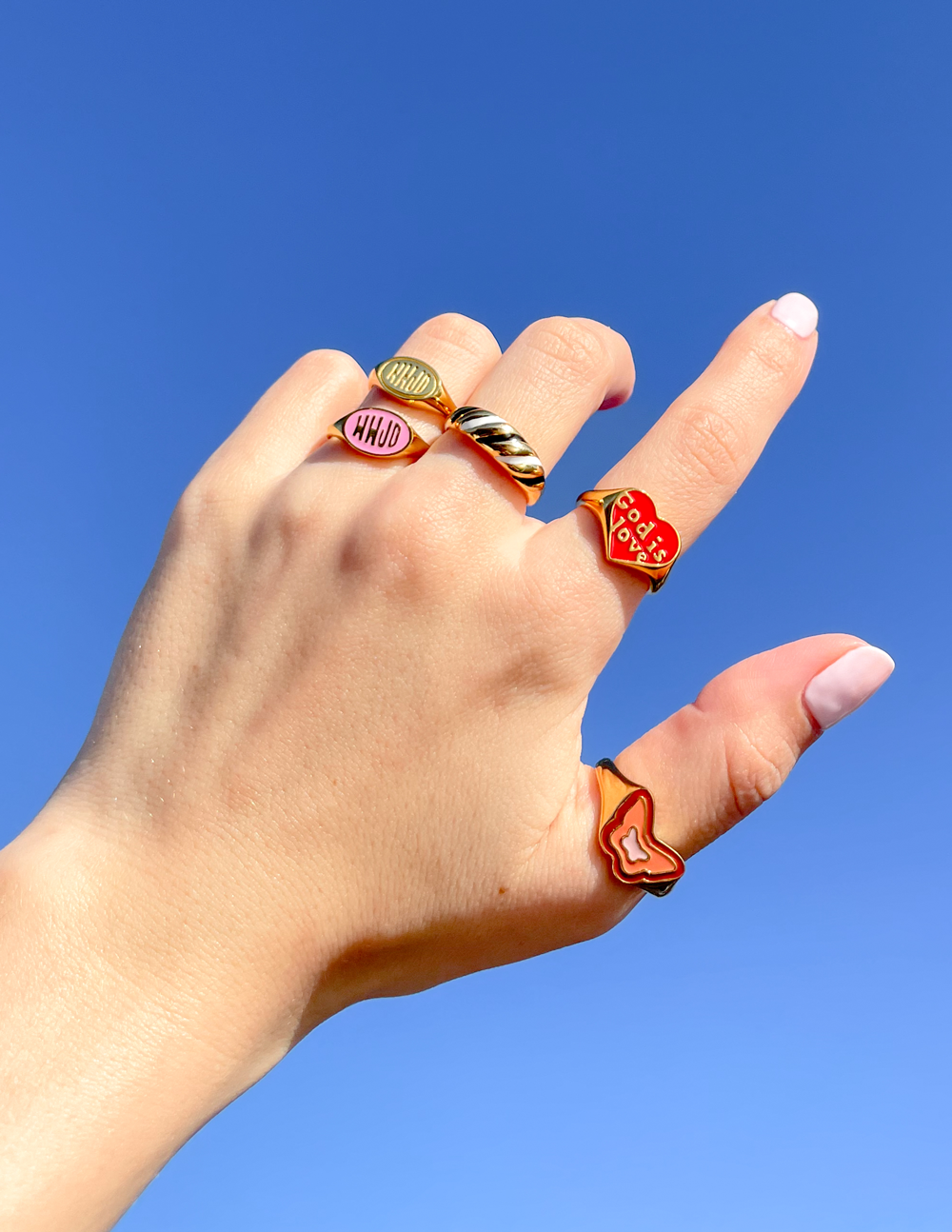 Pink enamel WWJD ring on finger, gold-tone band with pink oval center