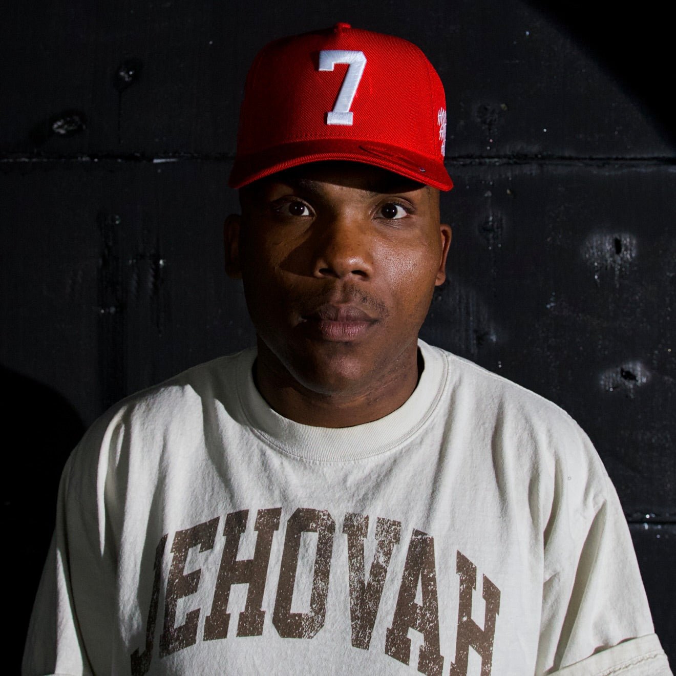 Red snapback cap worn by model with centered white '7' logo