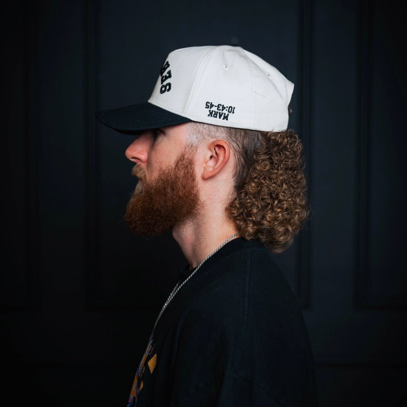 Cream-and-black snapback cap with side embroidery, worn from the back profile.