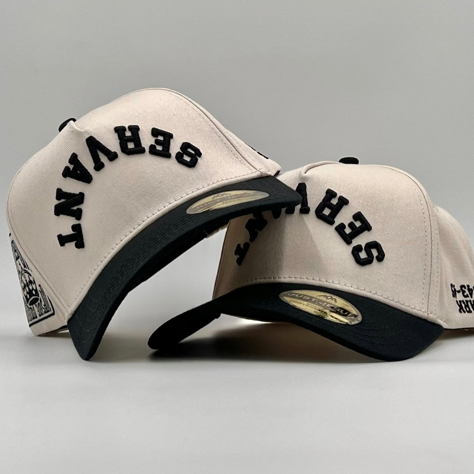 Cream and black snapback cap with black embroidered text and curved brim, adjustable strap