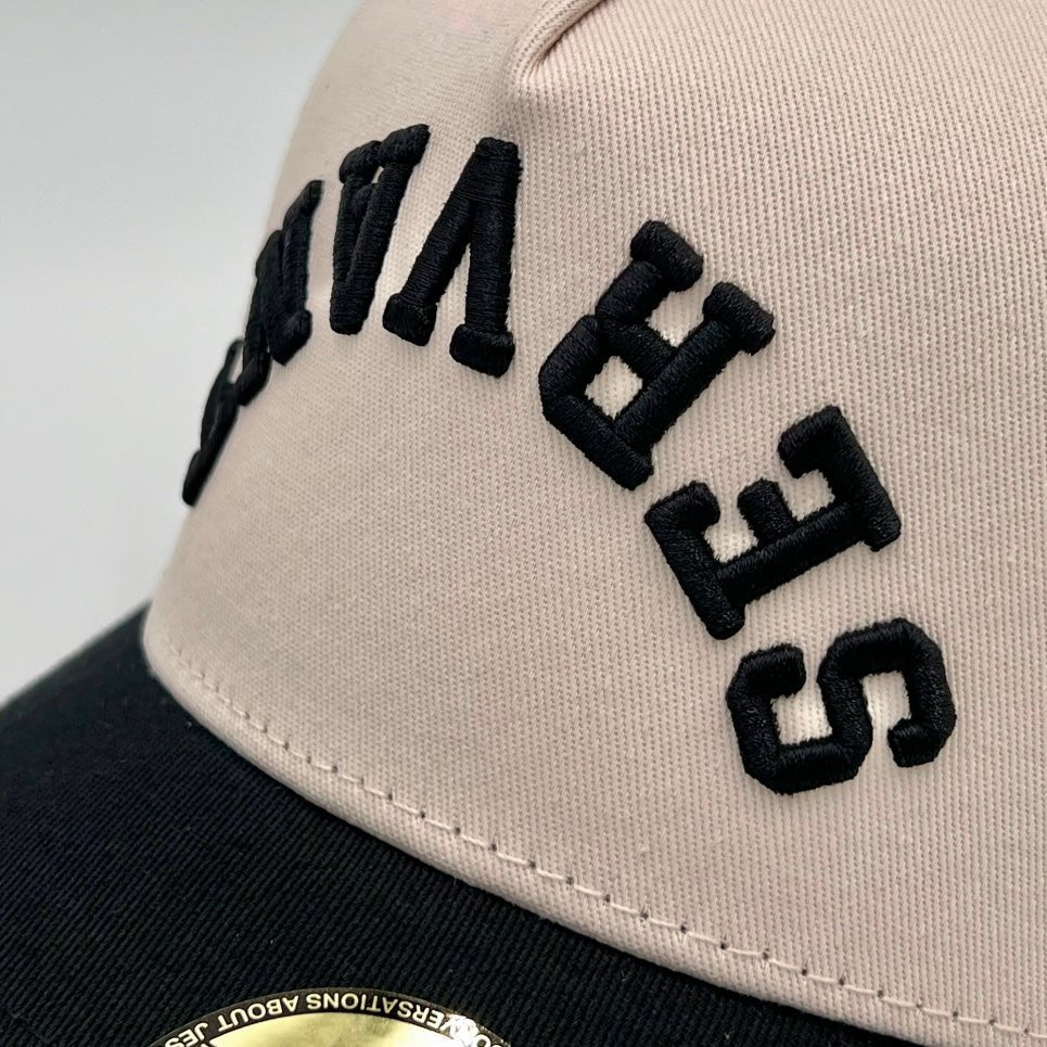 Close-up of cream snapback cap panel with black embroidered lettering.