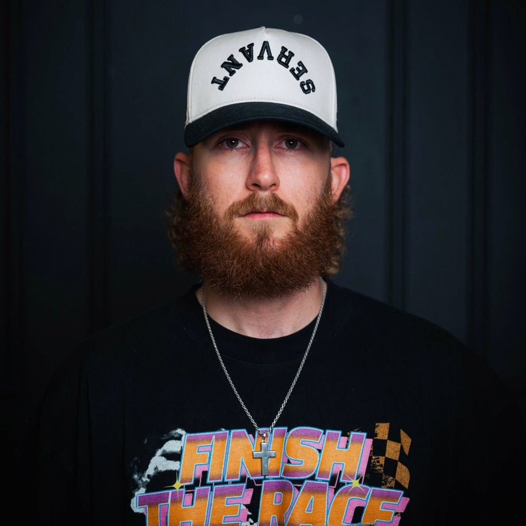 Cream-and-black snapback cap worn by a model with front embroidered text.