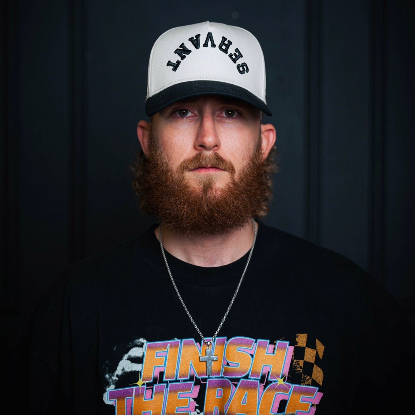 Cream-and-black snapback cap worn by a model with front embroidered text.