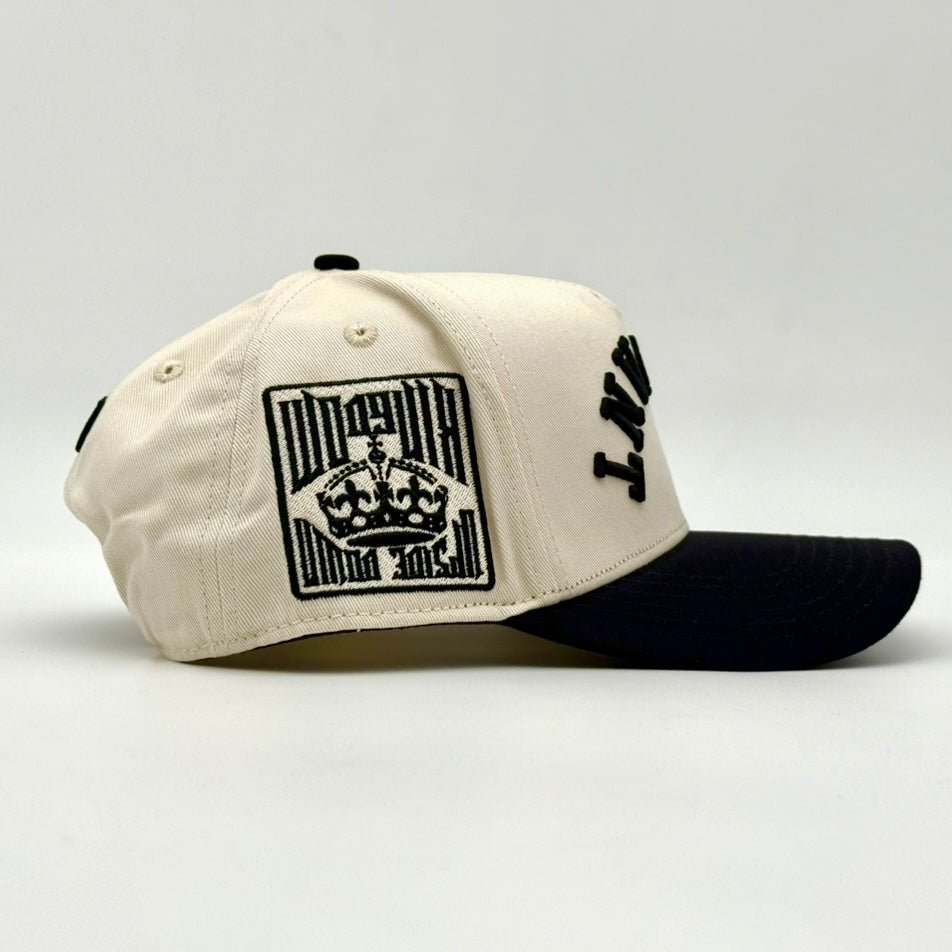 Cream snapback cap with rectangular front graphic and black brim, side view.