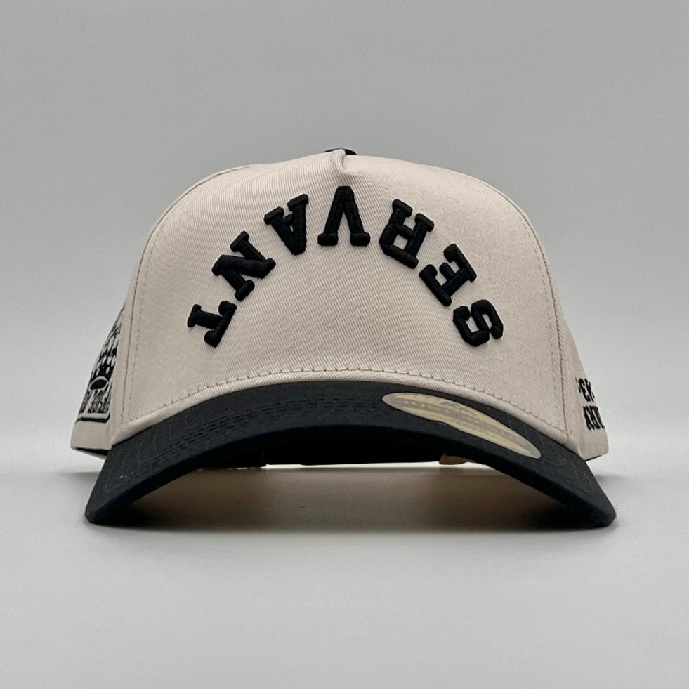 Cream snapback cap with black arch embroidery and dark brim, front view.