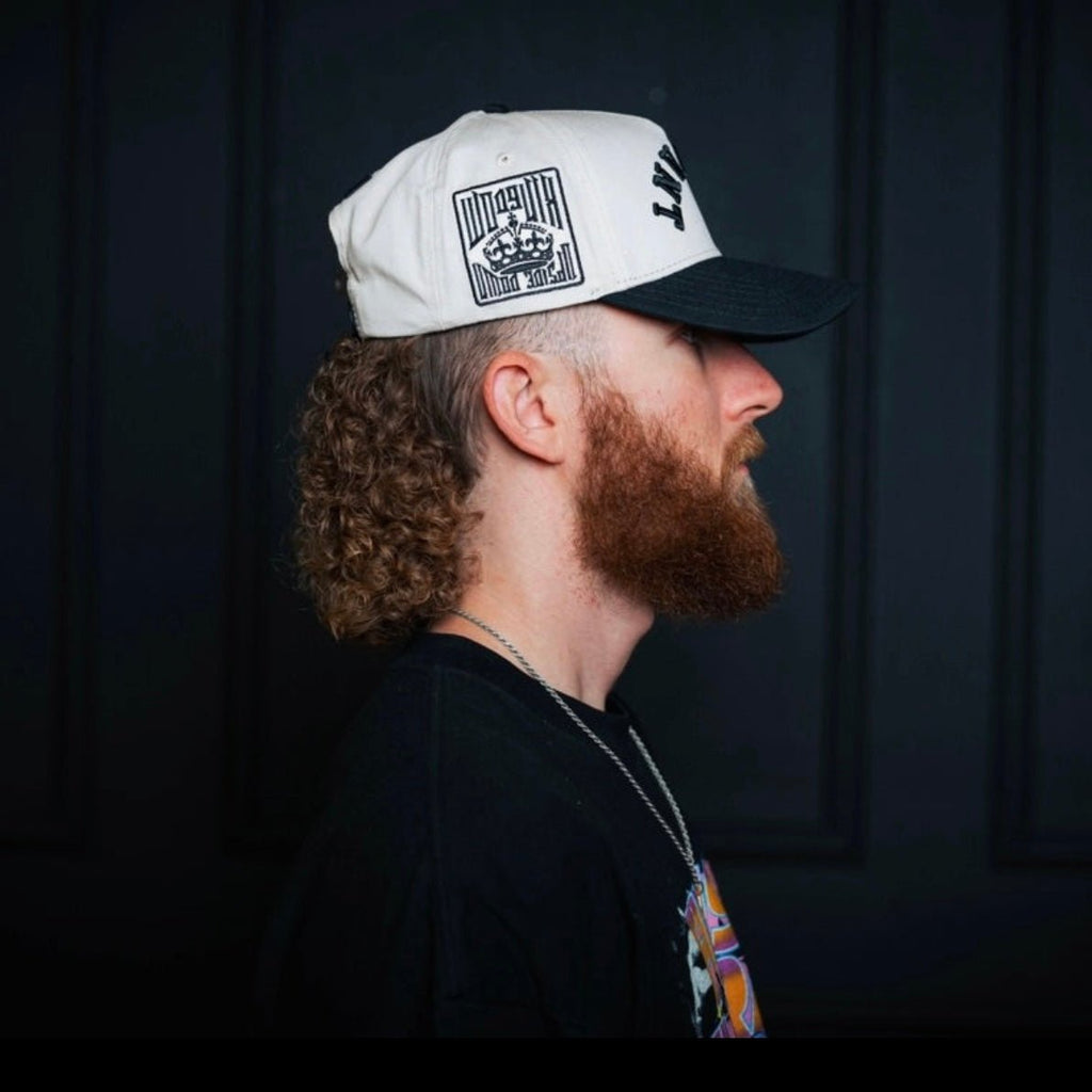 Cream snapback cap with black side and front prints, worn in profile.