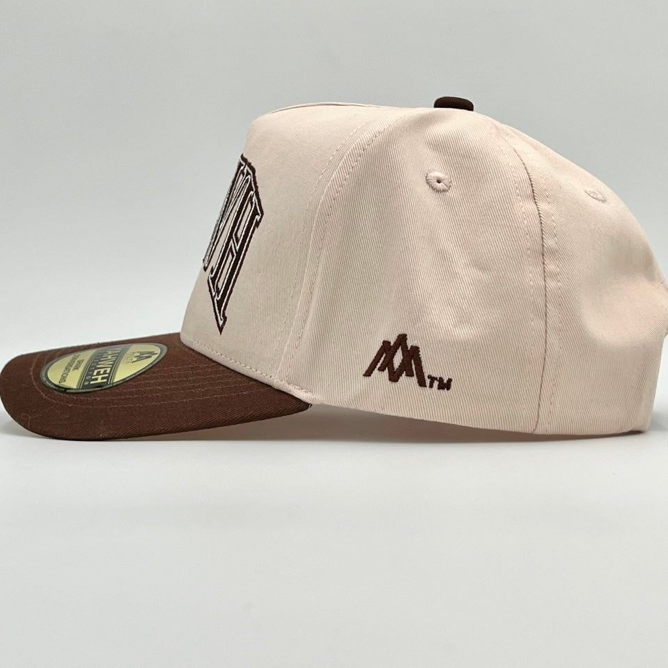 Cream snapback cap side view with small logo marks and brown brim