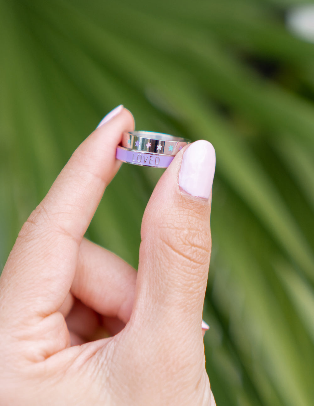 Lavender enamel ring on finger with LOVED lettering on the top band