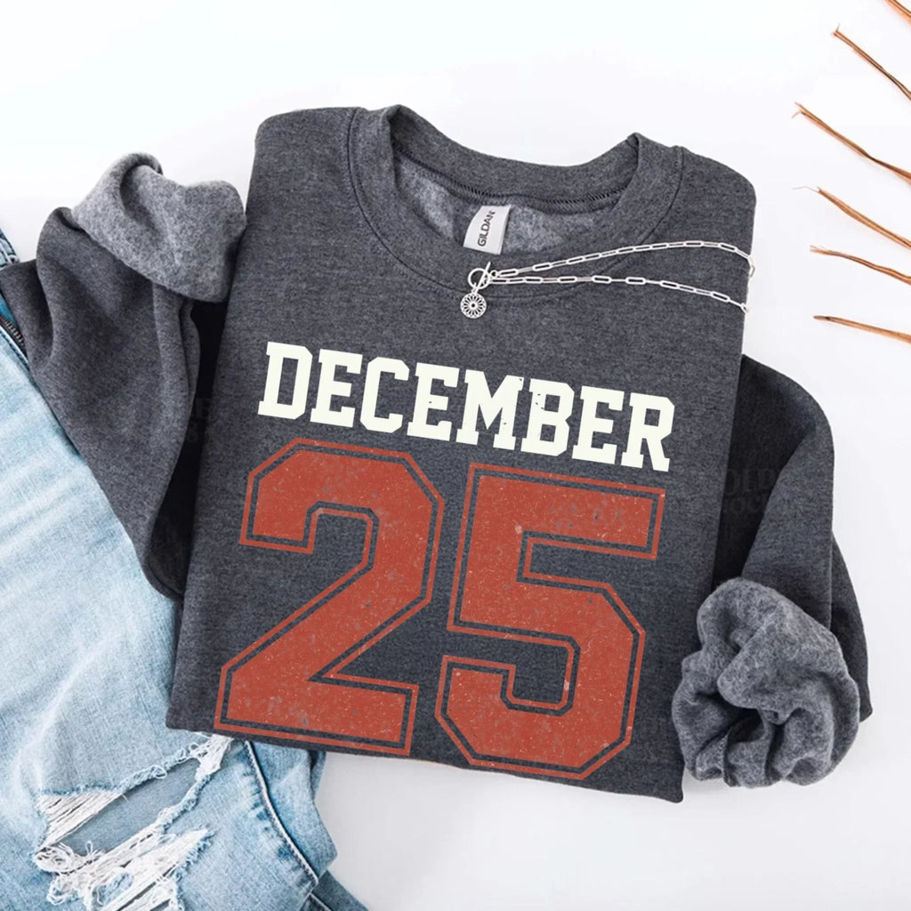 Dark gray crewneck sweatshirt with “DECEMBER 25” graphic and silver chain detail.