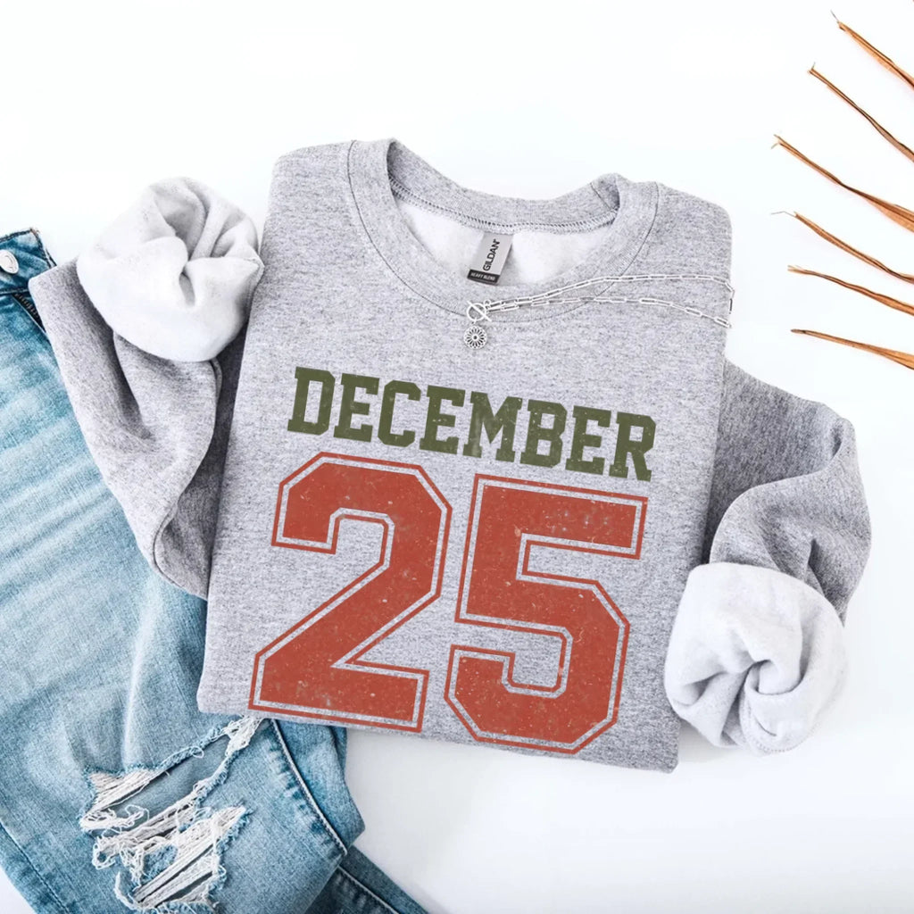 Light gray crewneck sweatshirt with “DECEMBER 25” graphic and silver chain detail.