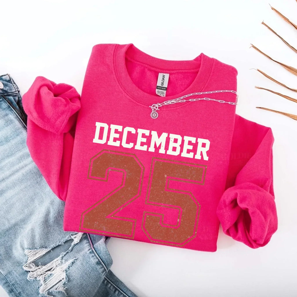 Magenta crewneck sweatshirt with “DECEMBER 25” graphic and silver chain detail at collar.