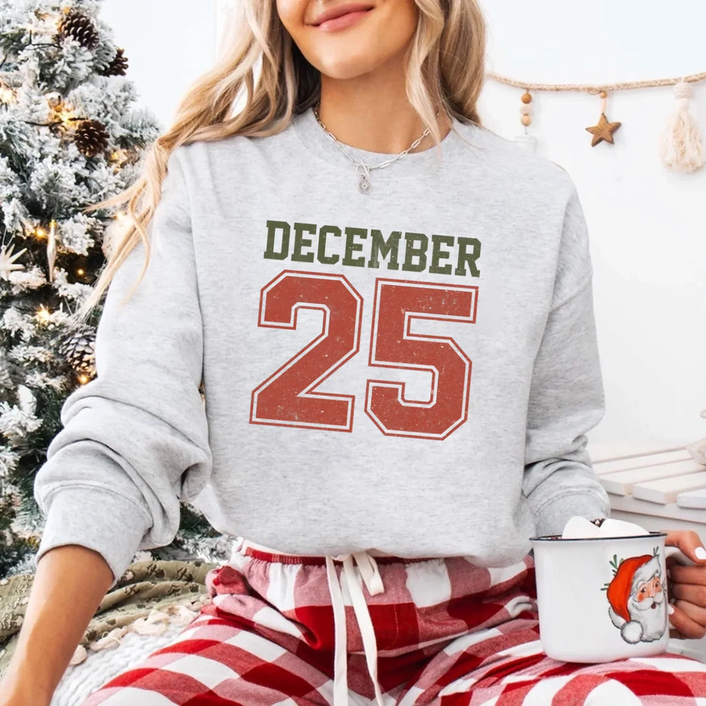Light gray crewneck sweatshirt with “DECEMBER 25” graphic and silver chain detail.