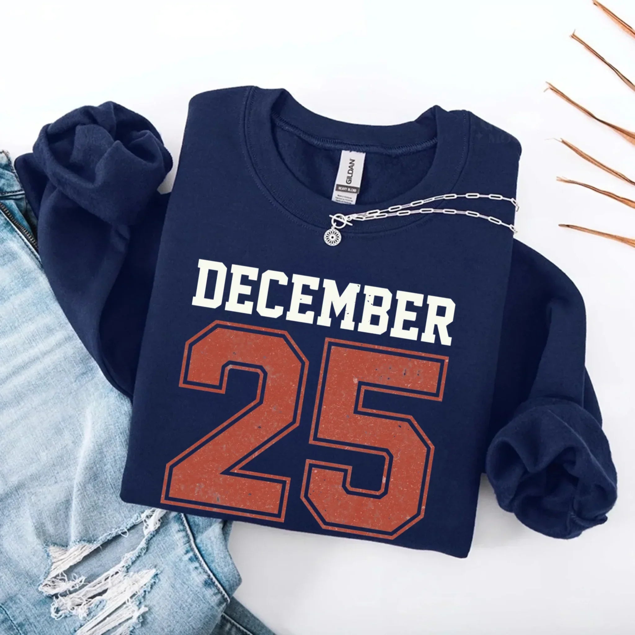 Navy crewneck sweatshirt with “DECEMBER 25” graphic and silver chain detail at neckline.