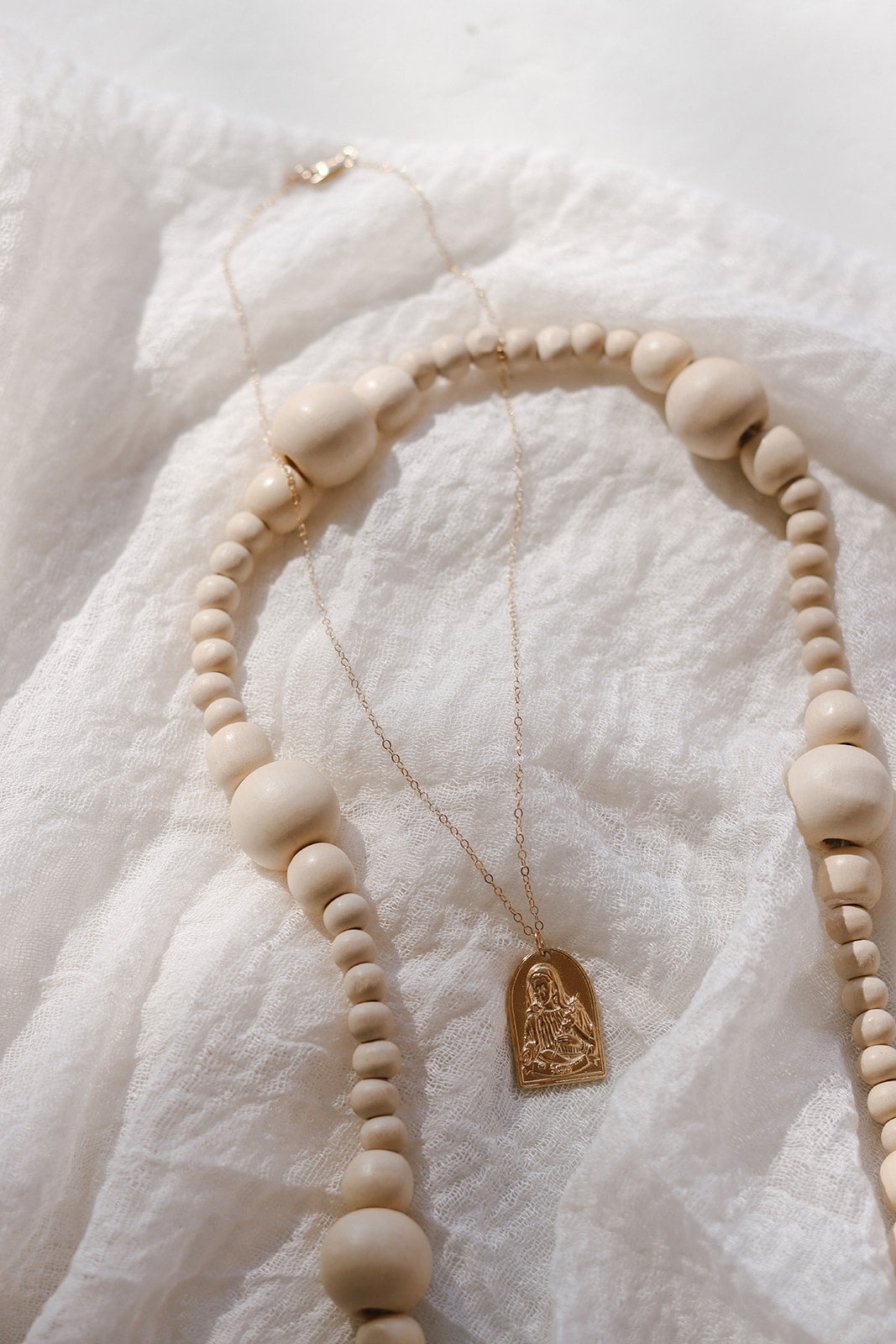 Gold-tone St. Catherine pendant necklace with white beaded collar and arch charm.