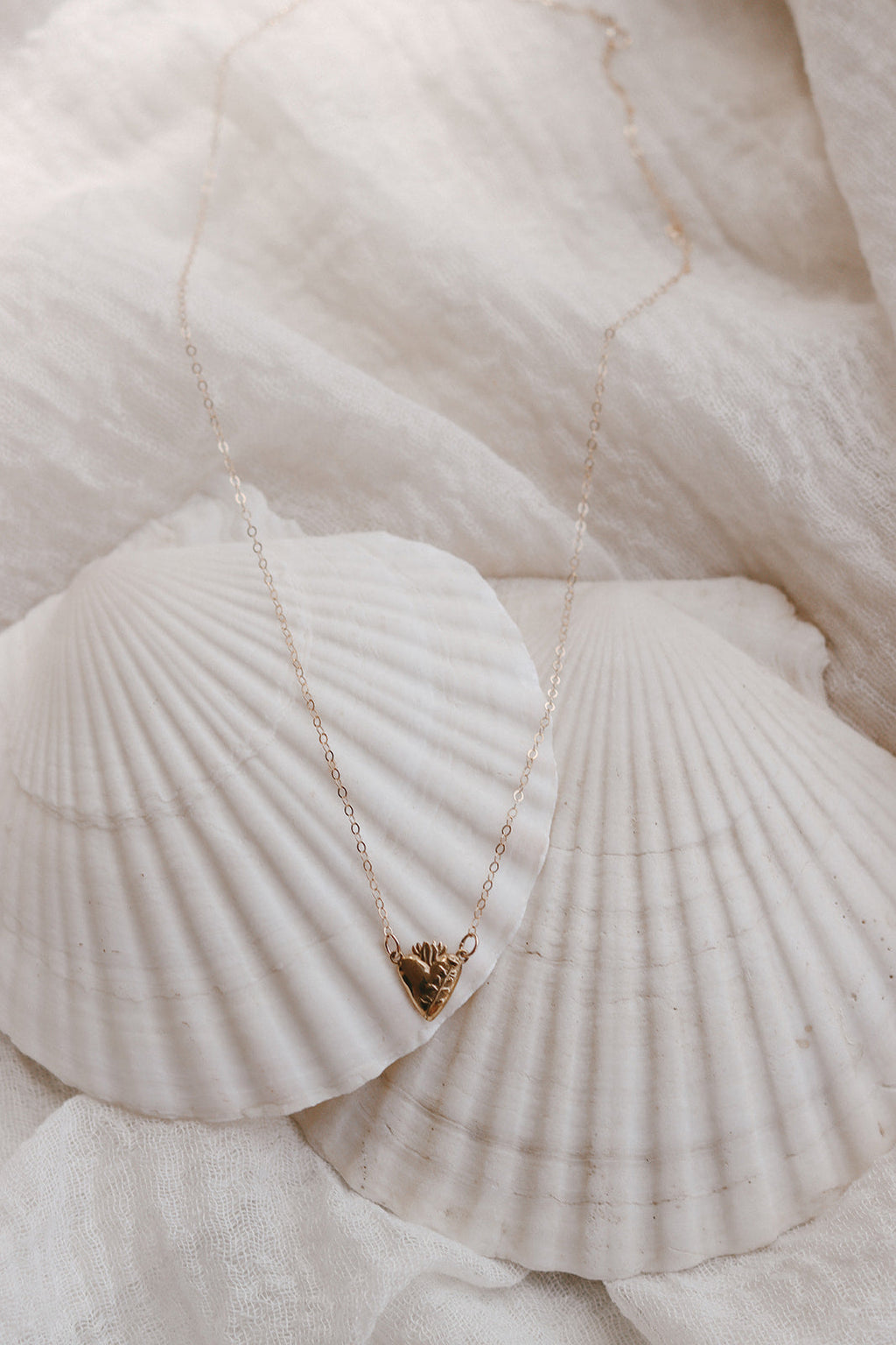 Gold heart pendant necklace on white seashells, delicate chain and floral top detail