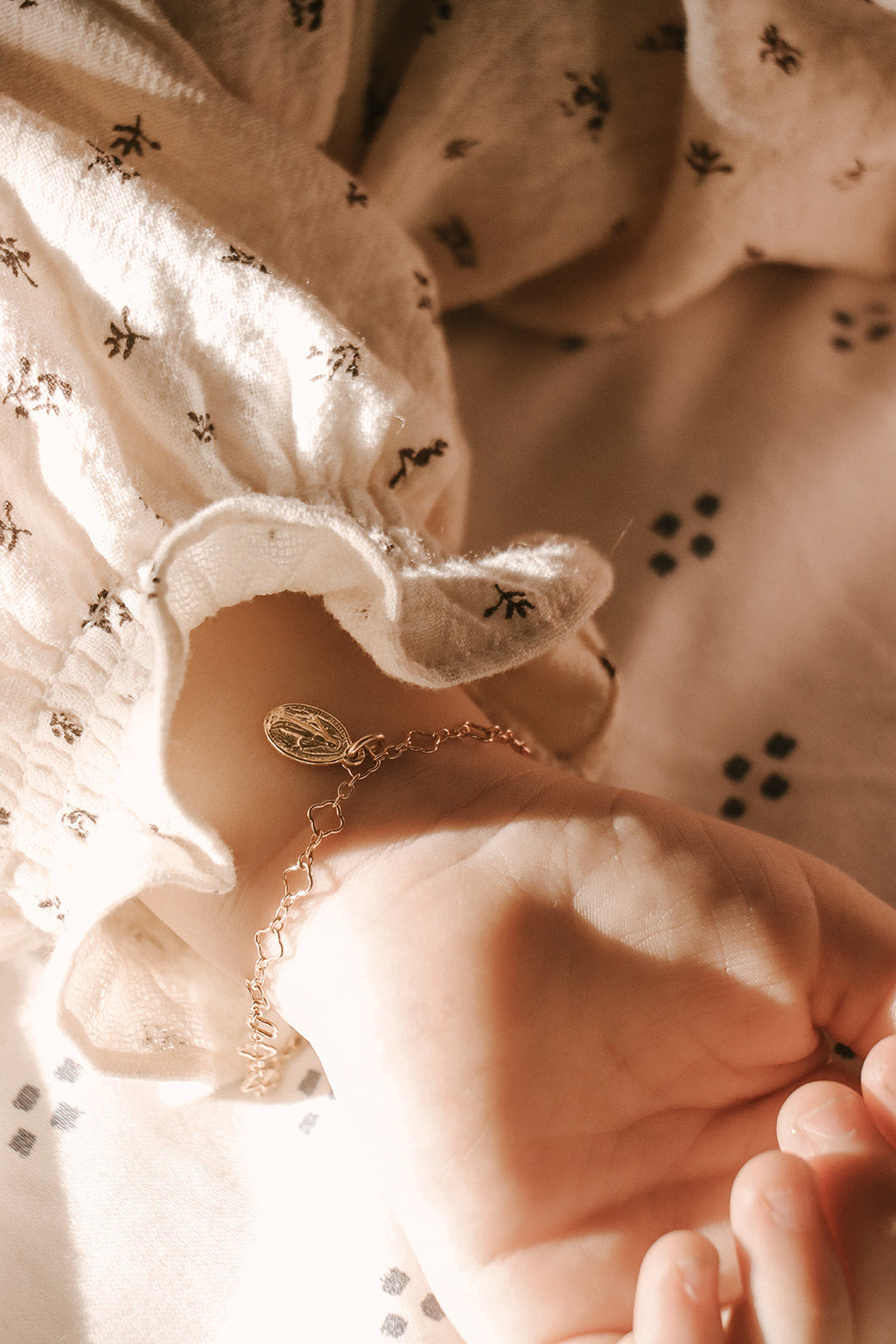 Gold-tone charm bracelet with oval medal charm near lace sleeve and hand