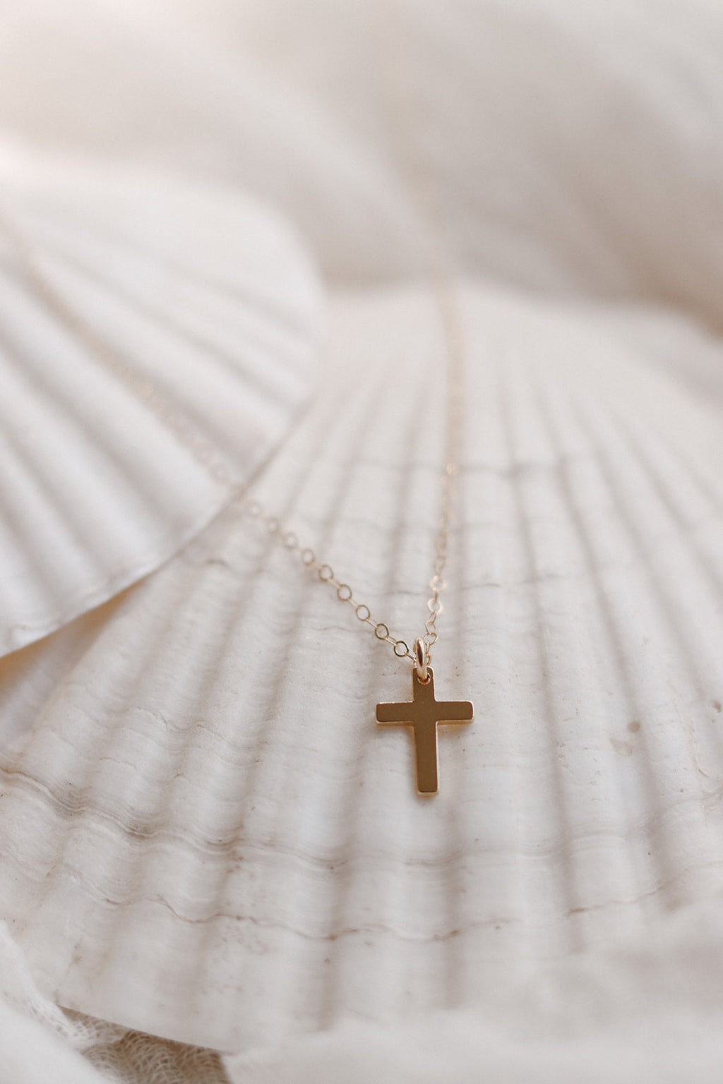 Gold cross pendant necklace on thin chain over white fabric, small cross charm