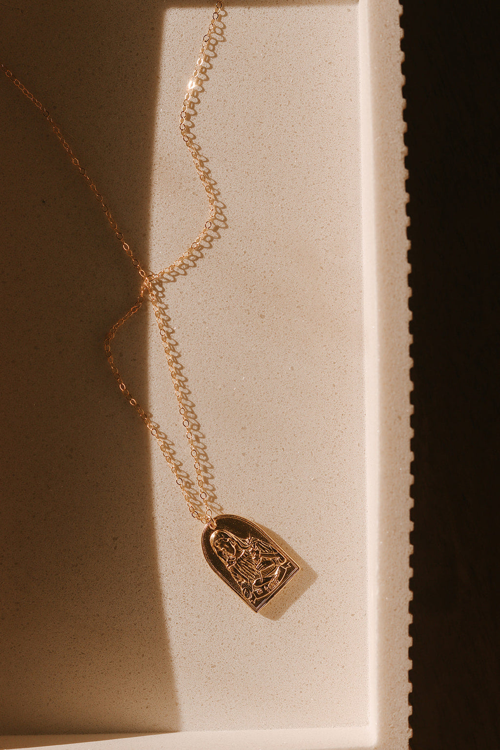 Gold-tone St. Catherine pendant necklace with arched portrait charm in display tray.
