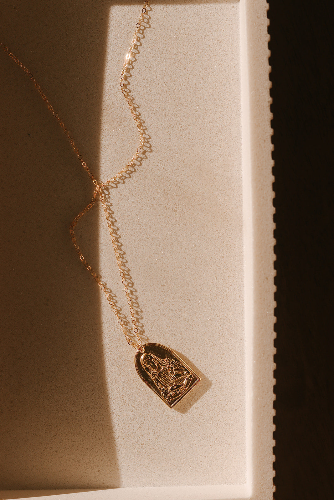 Gold-tone St. Catherine pendant necklace with arched portrait charm in display tray.