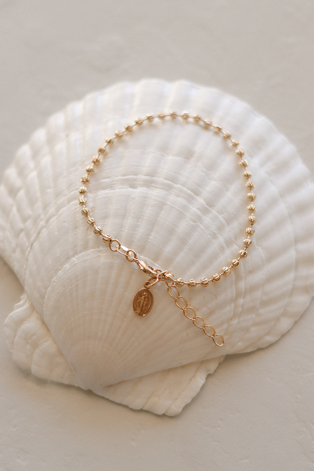 Gold-tone medal bracelet on white seashell with oval medal charm and extender.