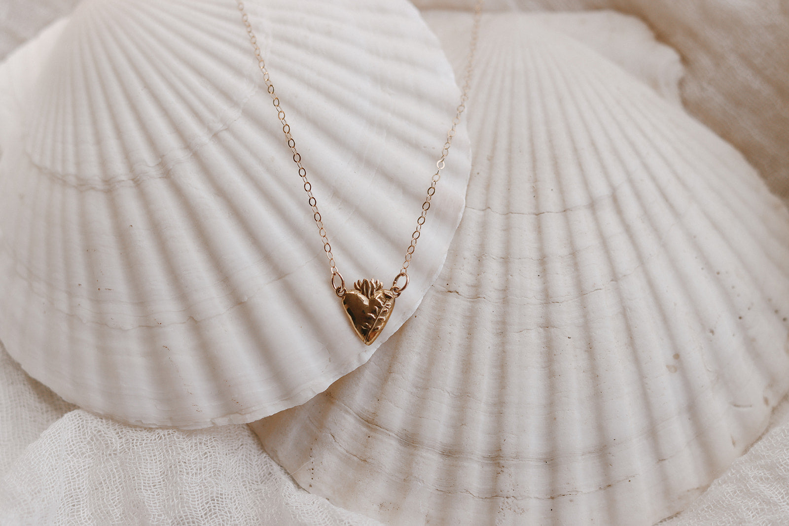 Gold heart pendant necklace on white seashells, delicate chain with floral detail