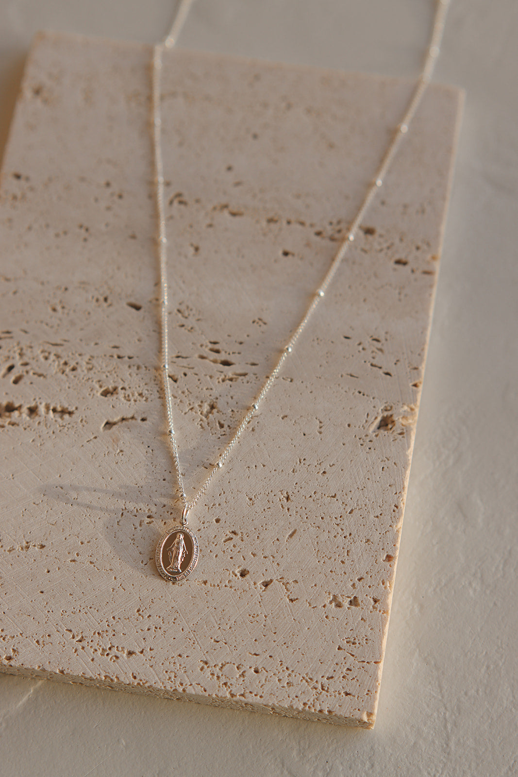 Silver oval medal pendant necklace with chain on textured display card
