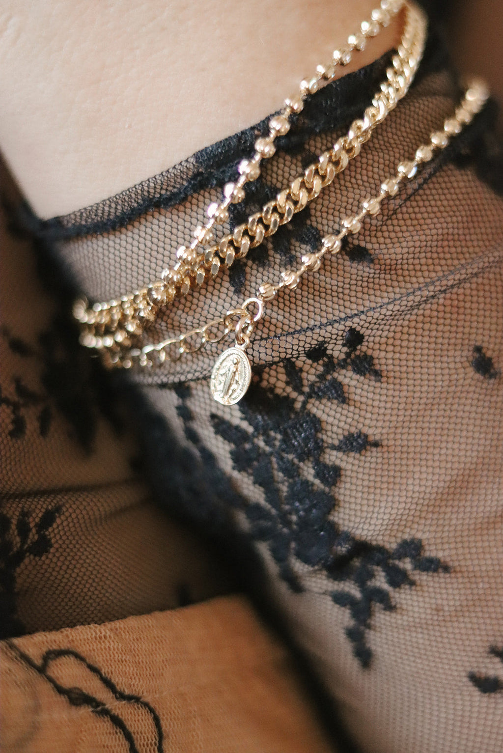 Gold-tone charm bracelet layered on wrist with oval medal pendant