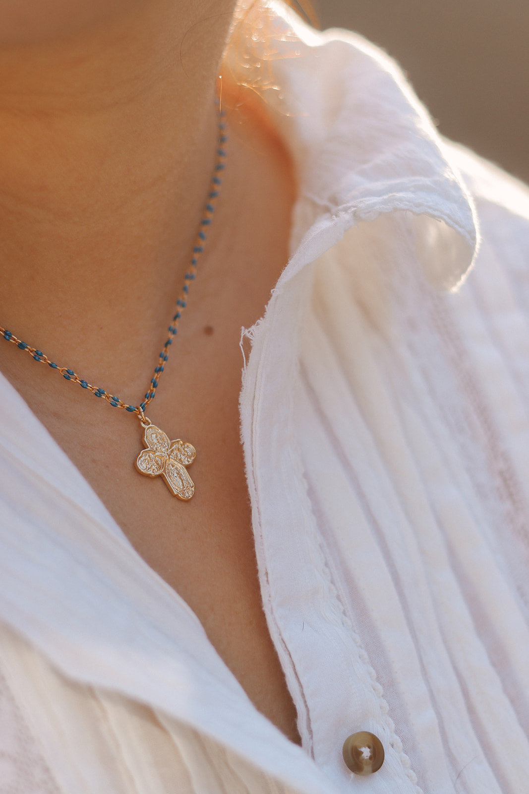 Four-way cross necklace with small floral cross pendant on blue bead chain