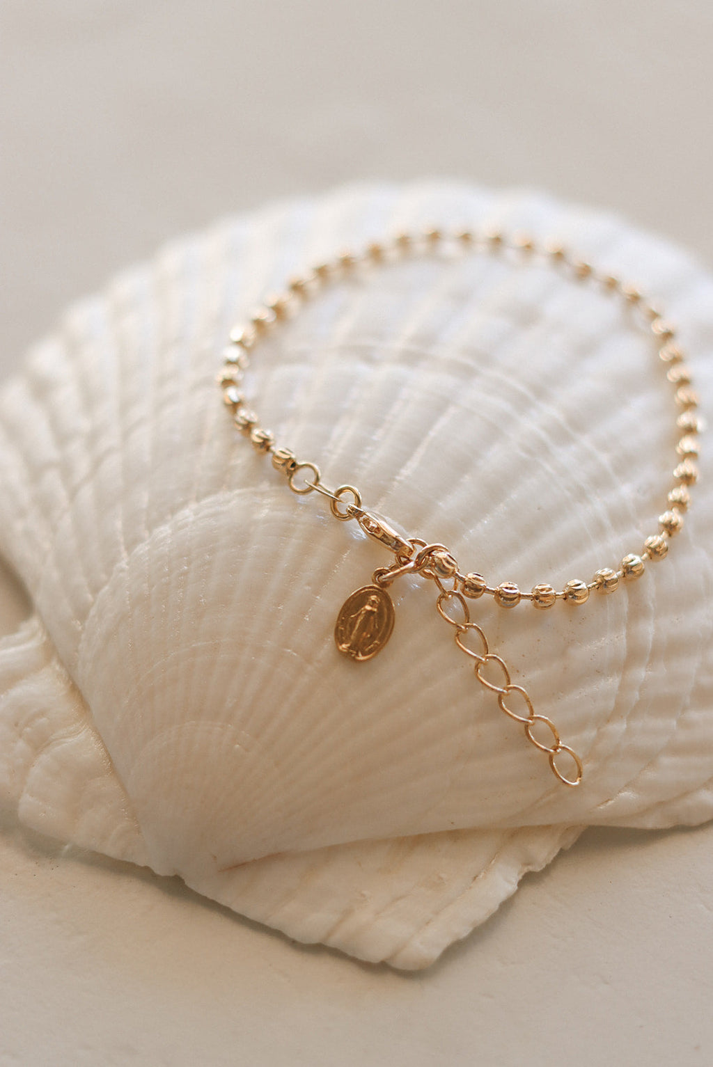Gold-tone medal bracelet with oval charm, link chain, and dangling extender.