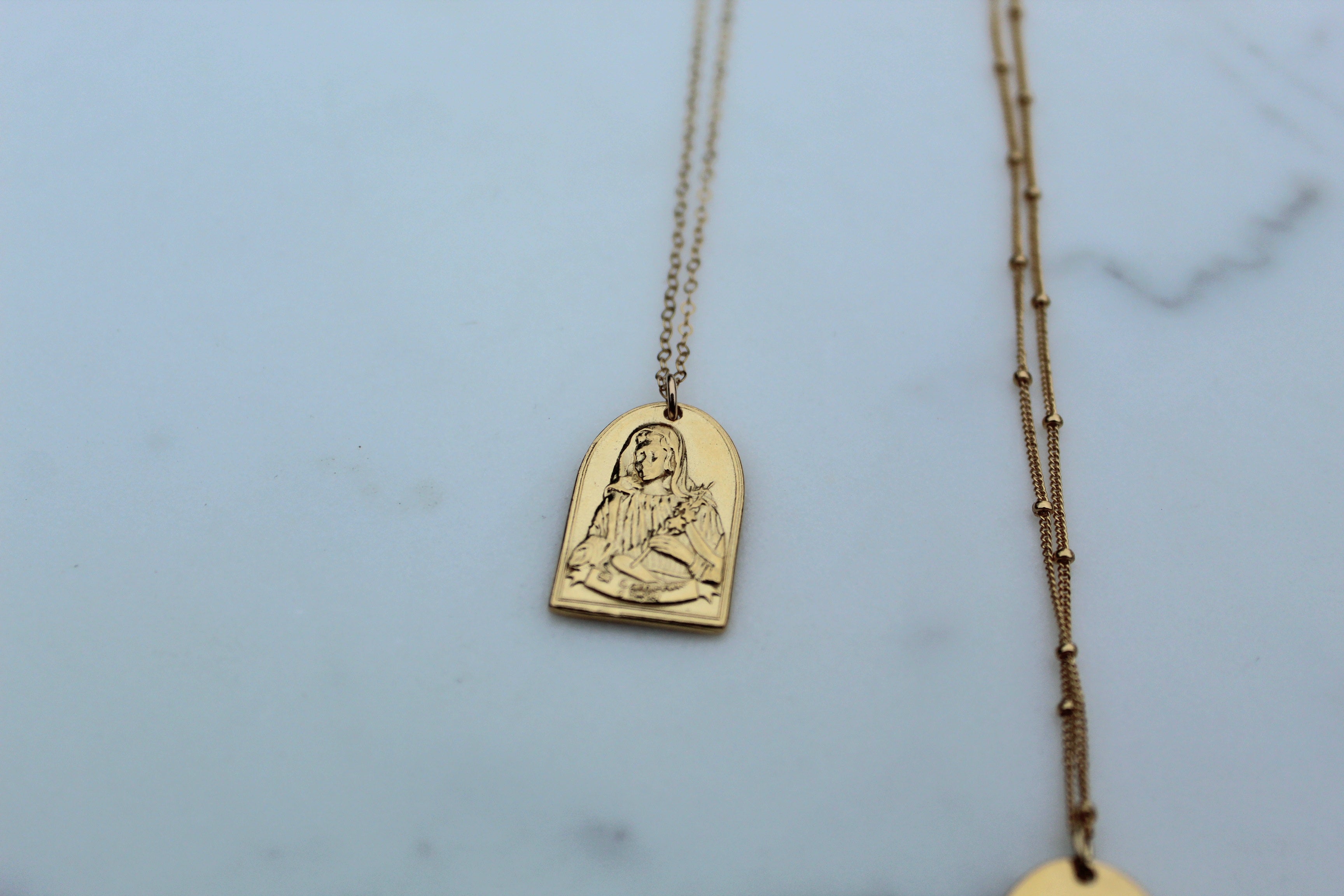 Gold-tone St. Catherine pendant necklace with arch portrait charm on chain.