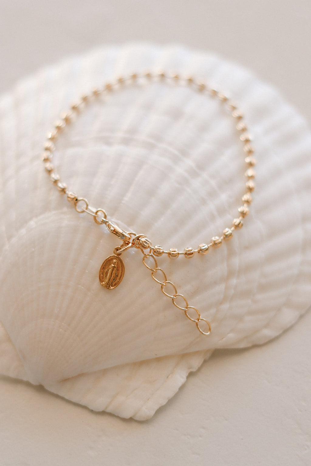 Gold-tone medal bracelet with oval medal charm and short dangling chain extender.