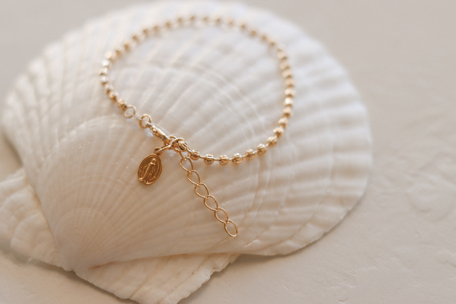 Gold-tone beaded bracelet with oval medal pendant and long dangling chain