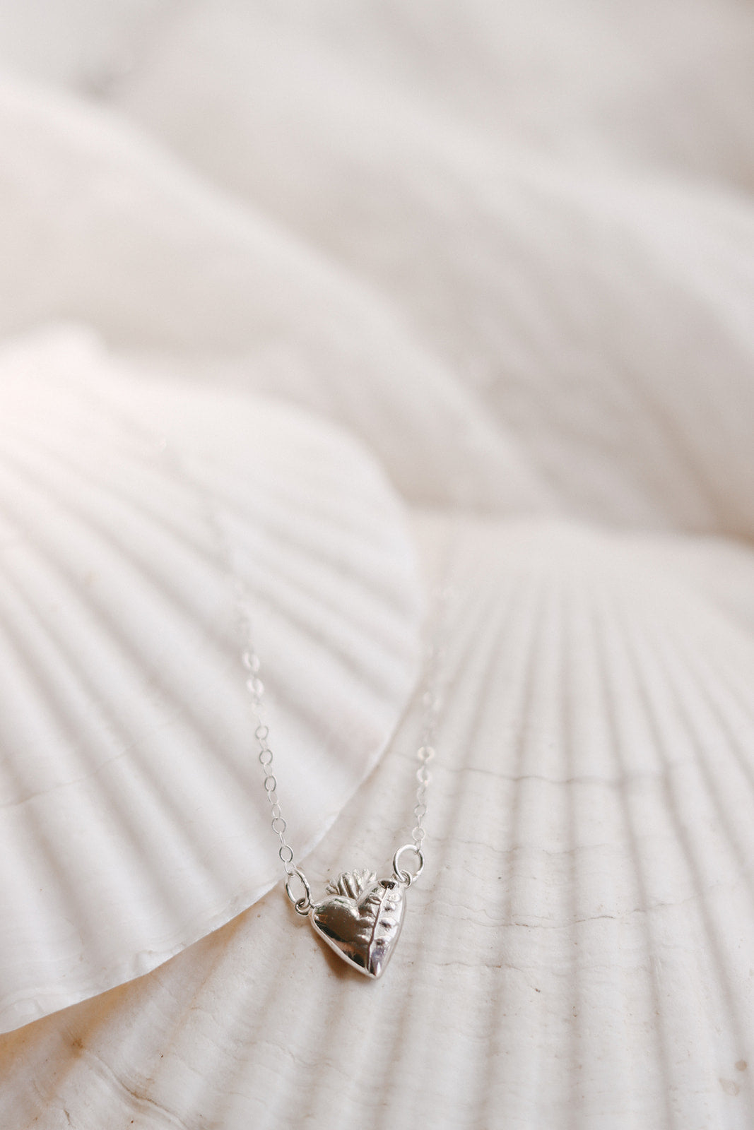 Sterling silver heart pendant necklace lying on fabric, small heart charm on chain