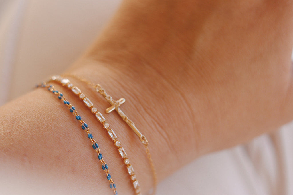 Layered bracelets on wrist: blue beaded band and gold cross charm bracelet