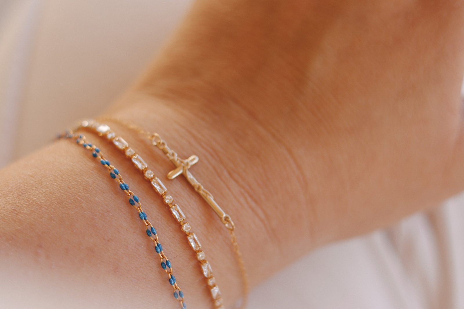 Layered bracelets on wrist: blue beaded band and gold cross charm bracelet