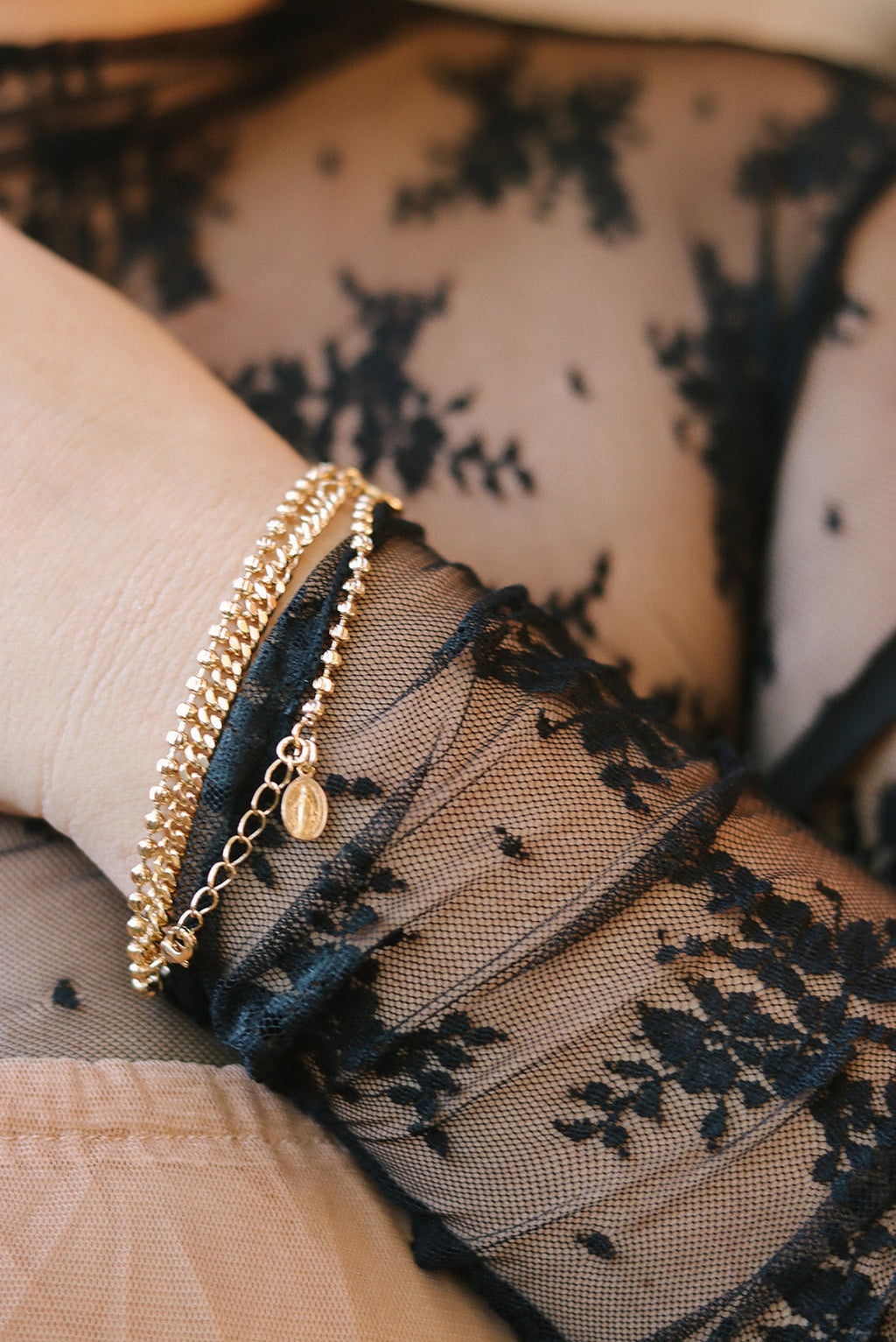 Gold-tone beaded charm bracelet on wrist with small oval medal pendant