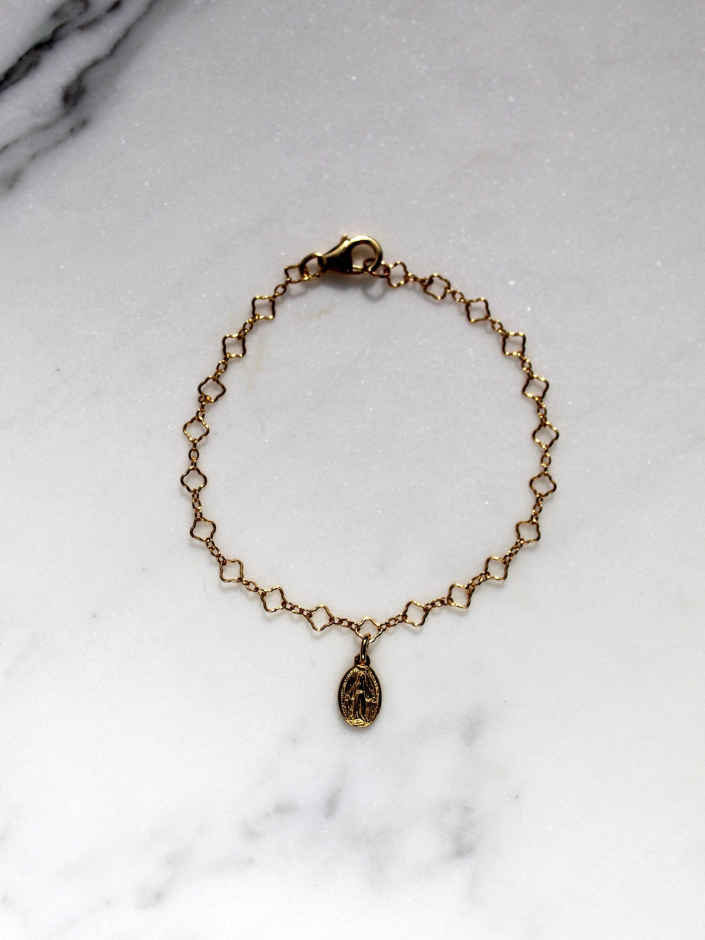 Gold children’s charm bracelet with oval medal pendant, shown flat on marble.
