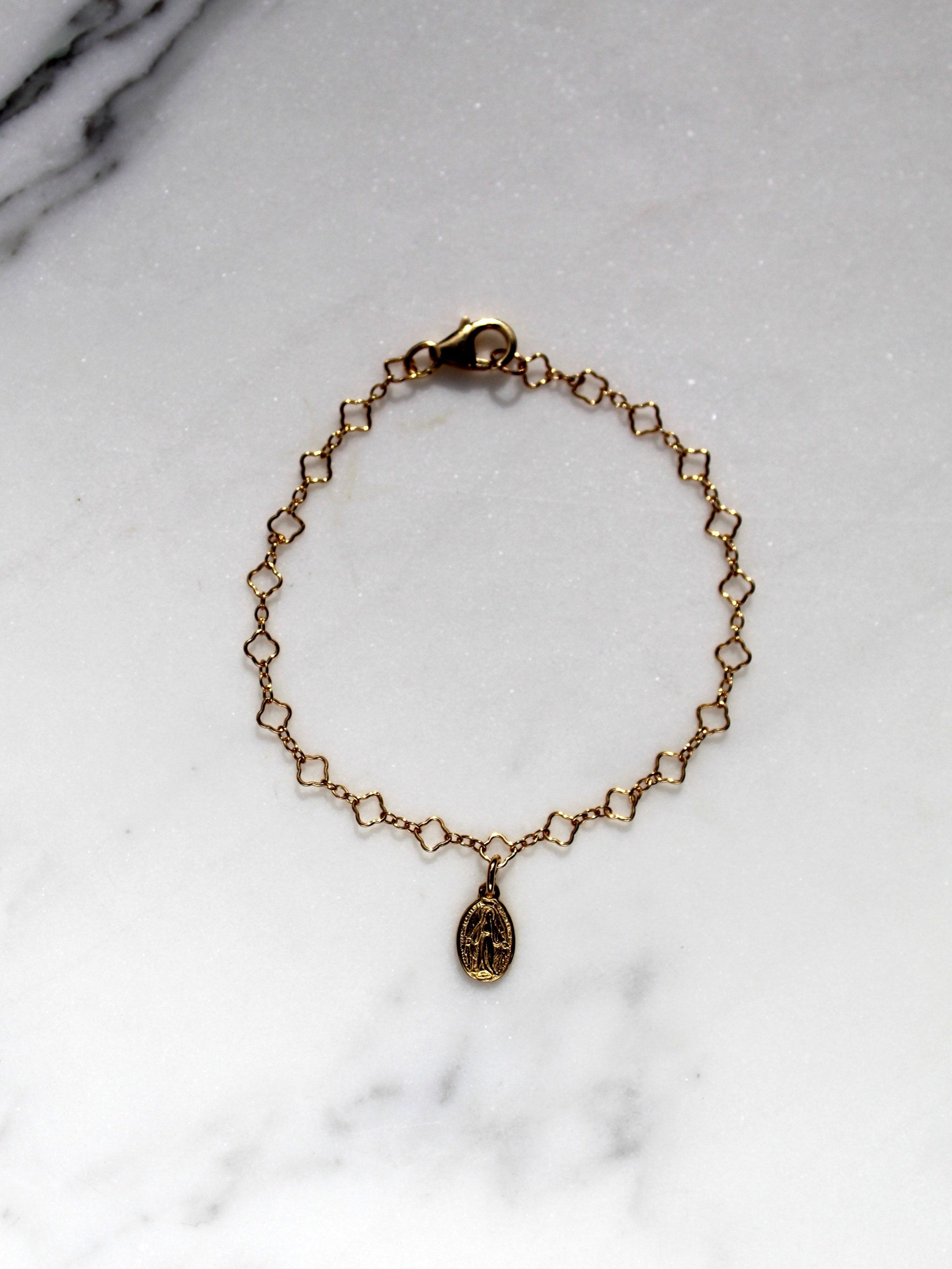 Gold children’s charm bracelet with oval medal pendant, shown flat on marble.