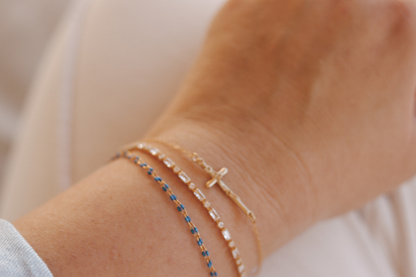 Gold-tone cross charm bracelet with blue beaded strand on a wrist